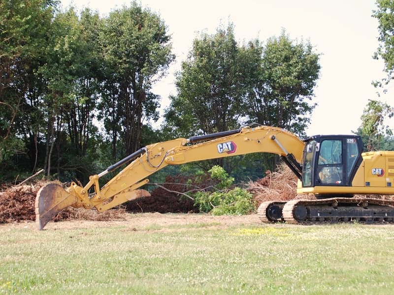A yellow excavator fitted with a mulching head working along a treeline.